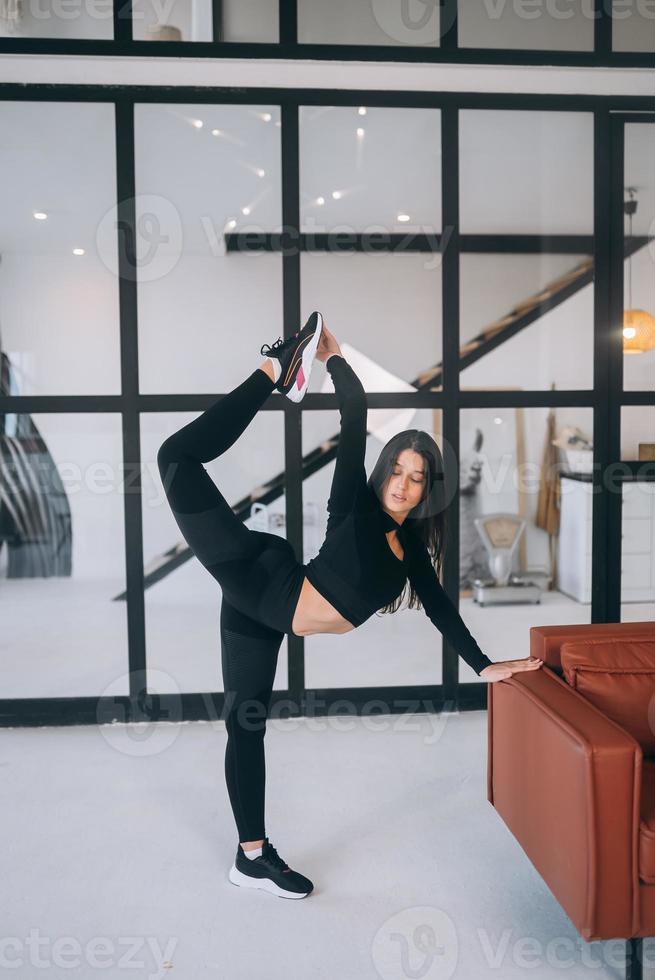 Young female wearing black sports suit stretching exercises indoors. photo