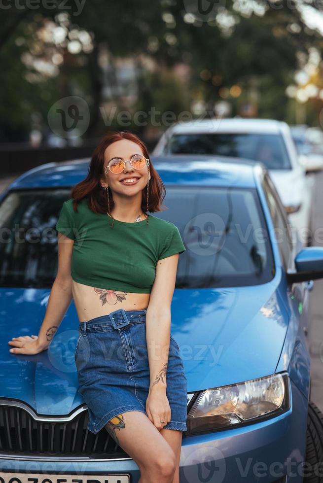 Beautiful girl sits on the hood of a blue car photo