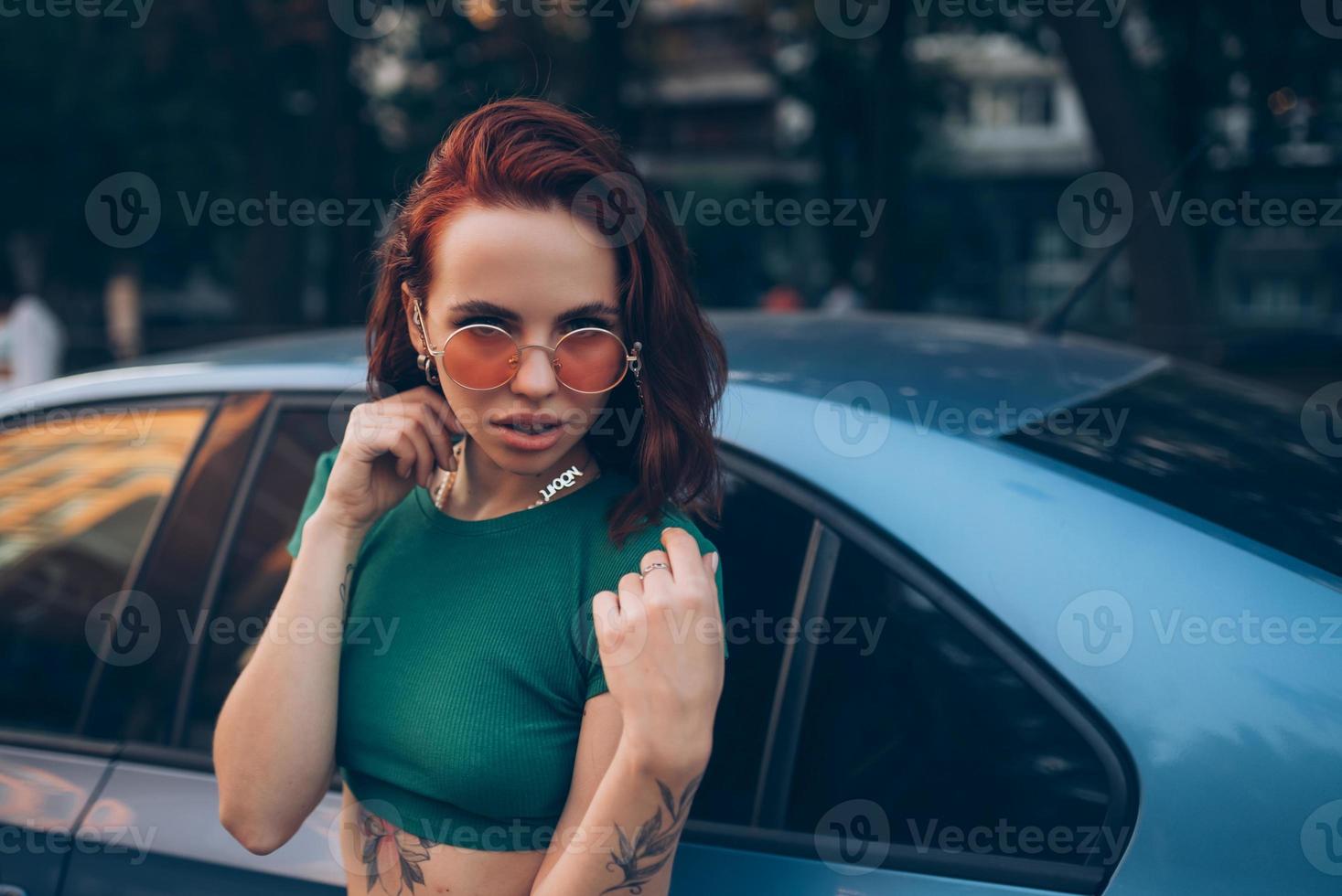 bella joven de moda con gafas posando cerca del coche foto