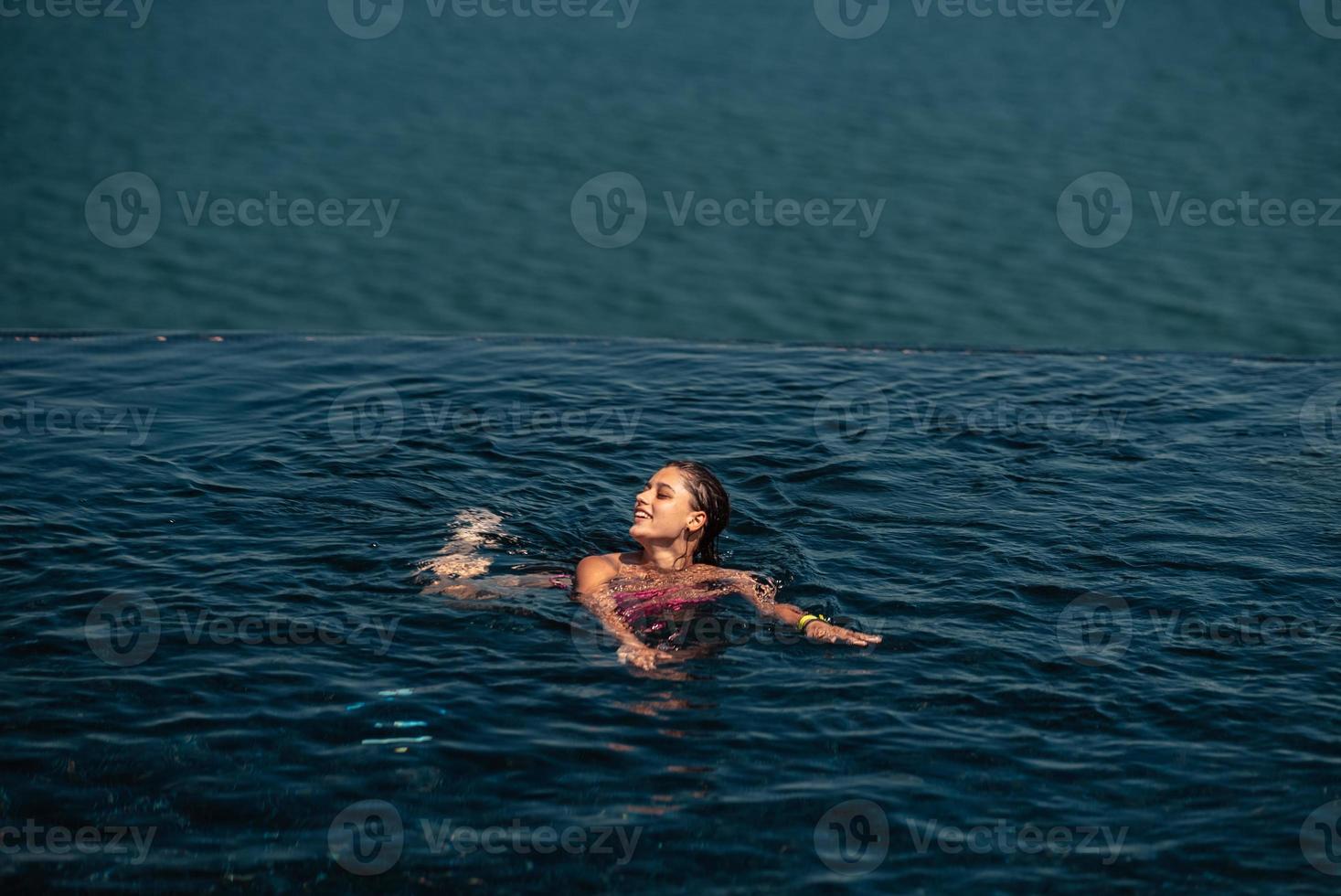 mujer feliz en traje de baño nadando en la piscina infinita frente al mar. foto