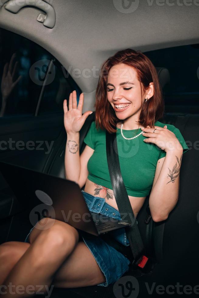 Beautiful woman is using laptop while sitting on back seat photo