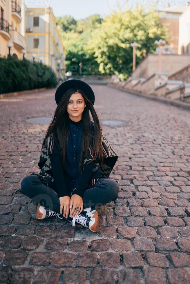 Young woman in hat sitting at city on cobblestone photo