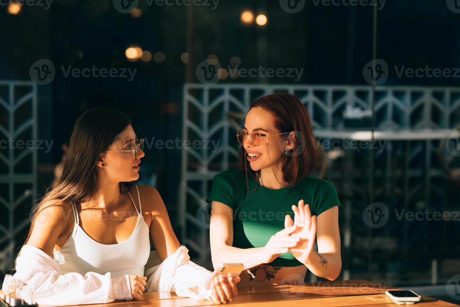 Girls using smartphones while sitting at the cafe outdoors photo