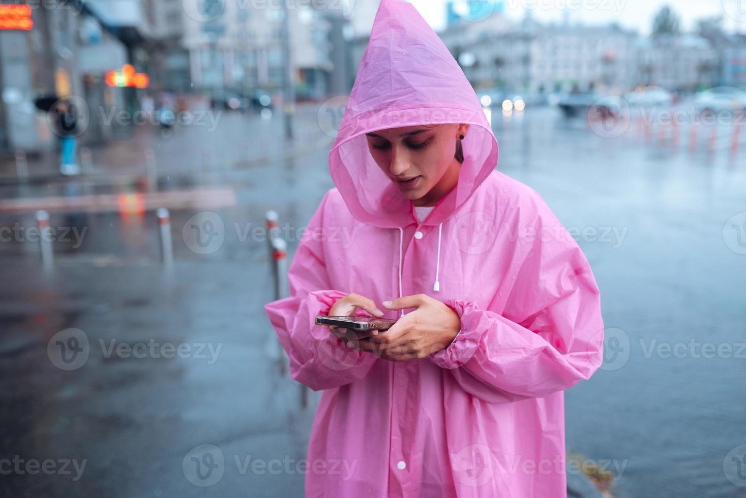 una mujer joven con un impermeable mirando el teléfono inteligente foto