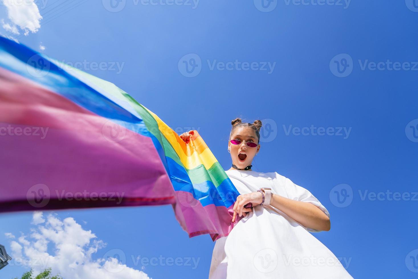 A young woman develops a rainbow flag against the sky photo