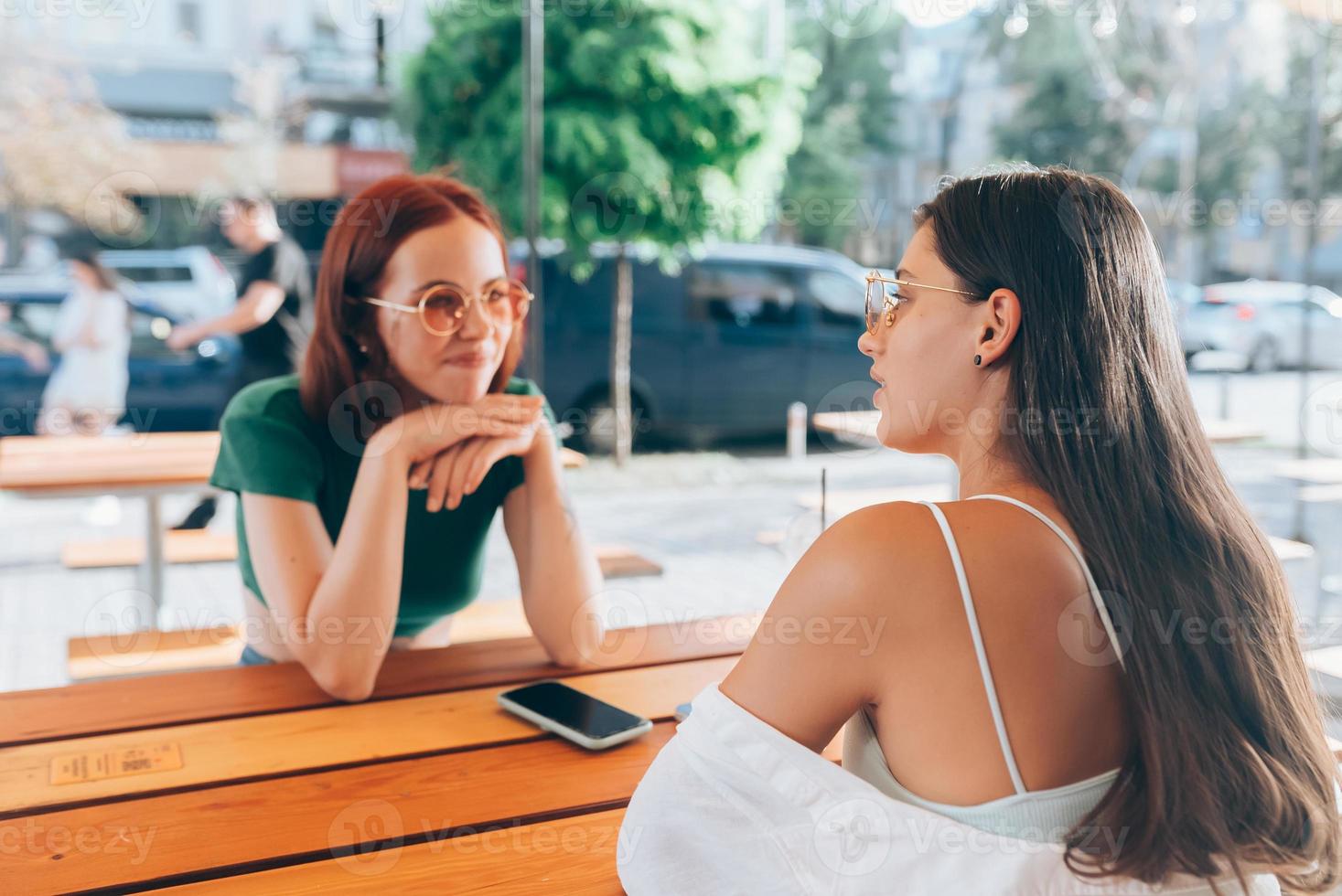Two pretty girlfriends talking while sitting in a bar outdoors photo