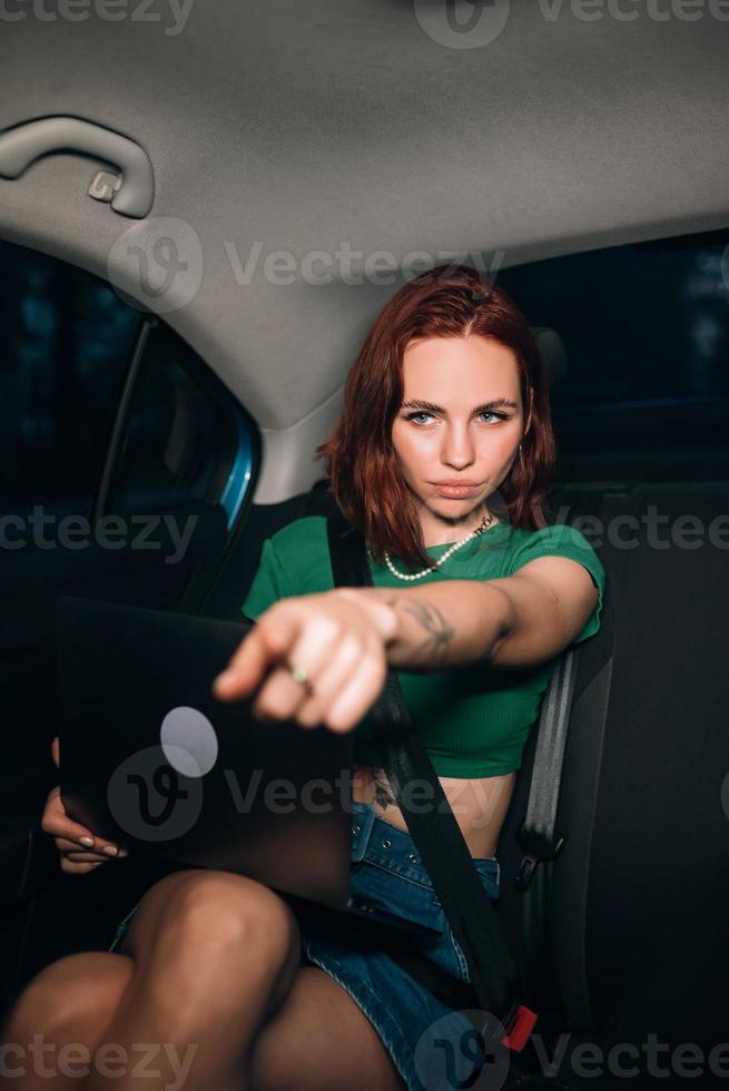 Beautiful woman is using laptop while sitting on back seat photo