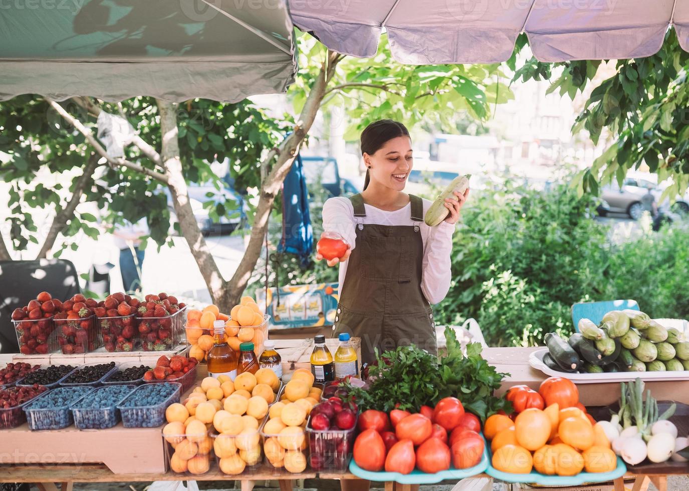 Young saleswoman holding zucchini and tomato in hands photo