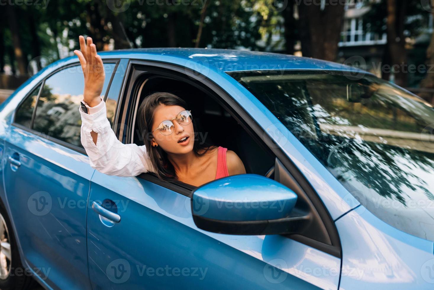 A young angry woman peeks out of the car window photo