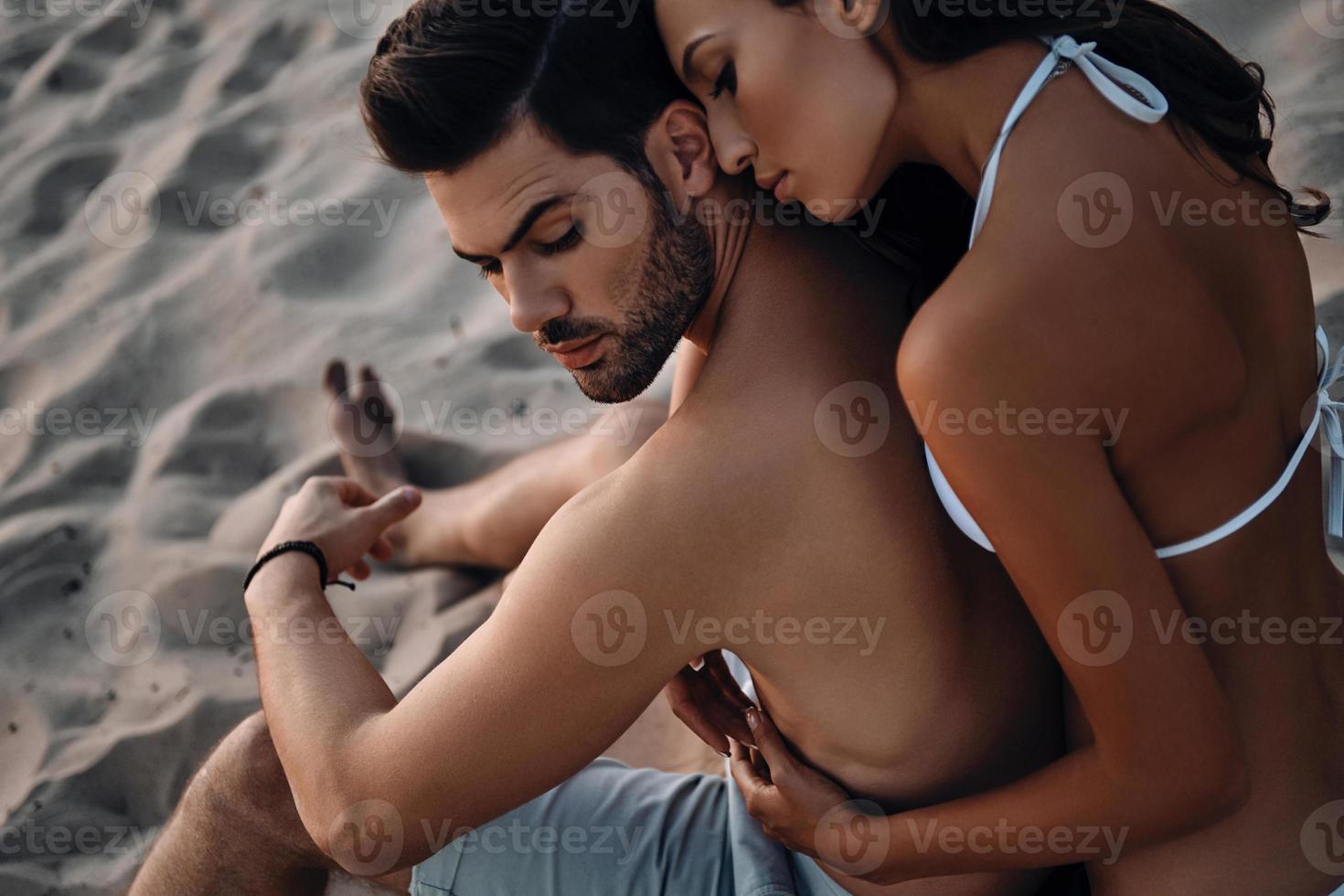 amar por siempre. vista superior de una hermosa joven abrazando a su guapo novio mientras se relaja en la playa foto