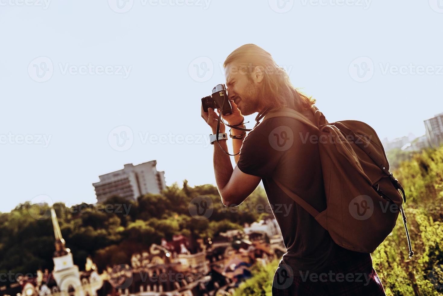 I must capture this Young man in casual clothing photographing the view while standing on the hill outdoors photo