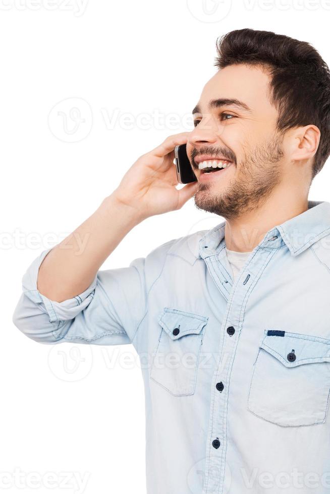 Good  talk. Portrait of cheerful young man talking on the mobile phone and smiling while standing against white background photo