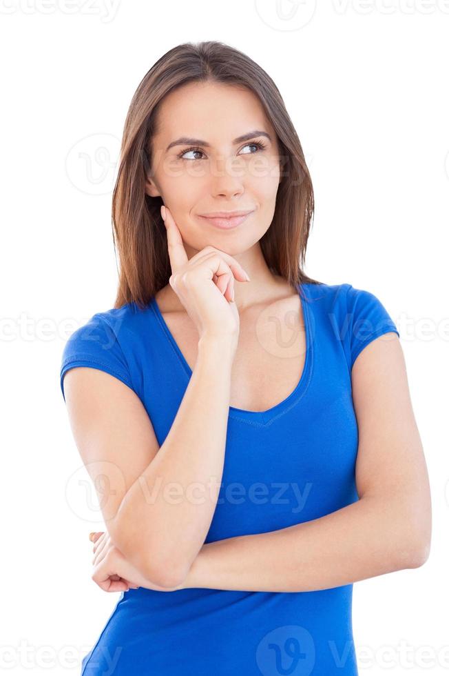 Thoughtful young beauty. Beautiful young woman holding hand on chin and looking away while standing isolated on white photo