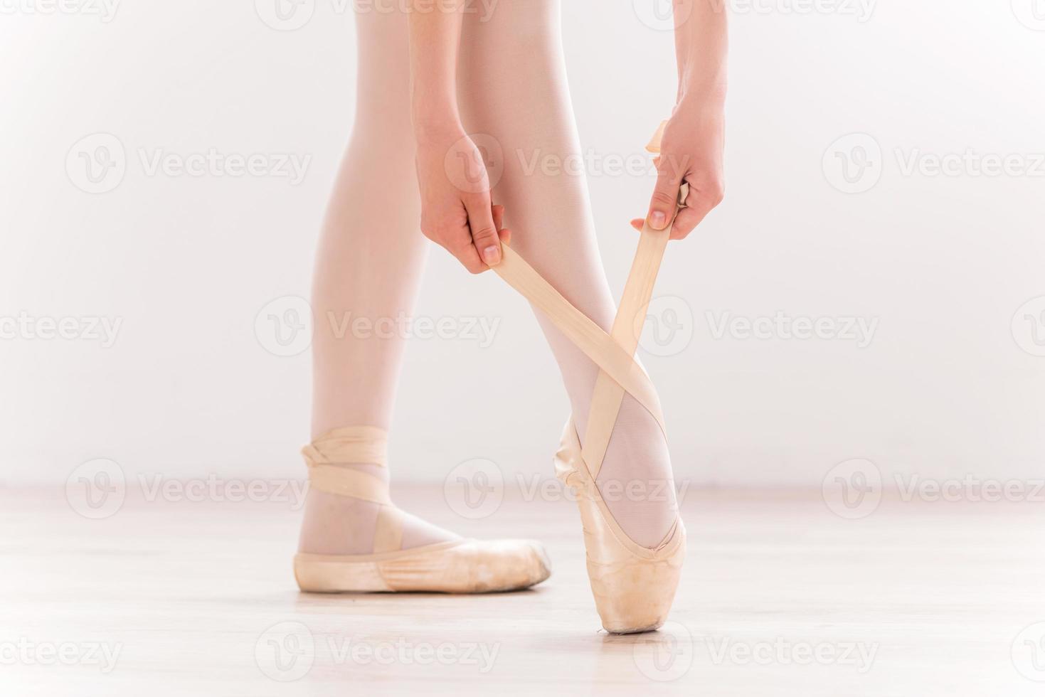 Tying her slippers. Close-up of ballerina wearing her slippers while standing on hardwood floor photo