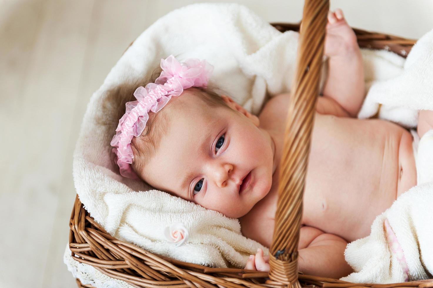 Baby in a basket. Top view of little baby lying in wicker basket and covered with towel photo