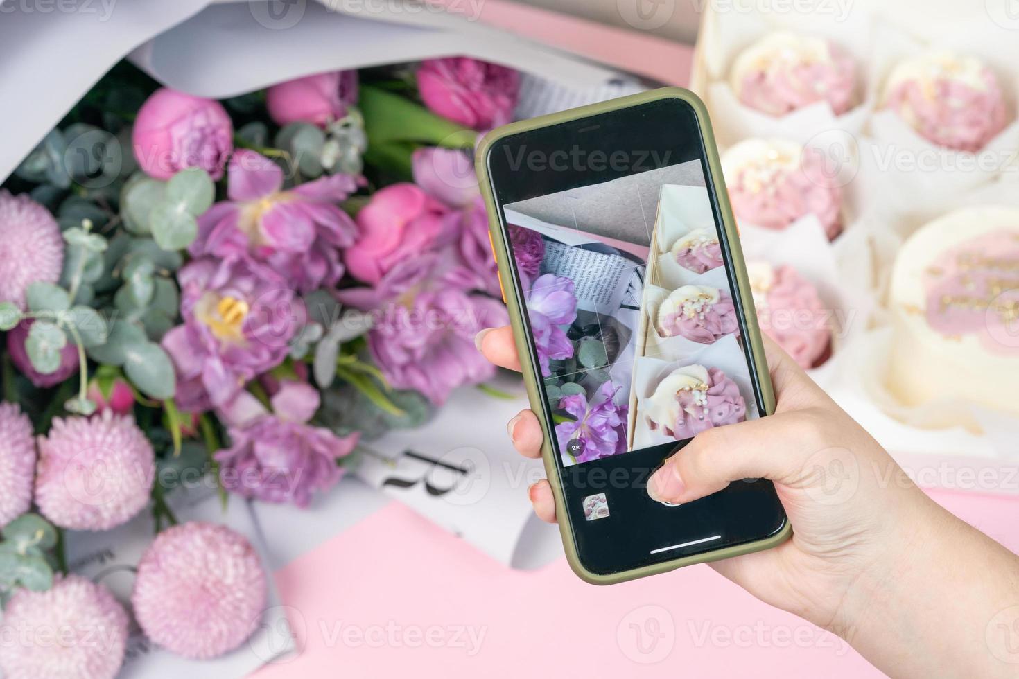 Photo on phone of freshly cupcakes and beautiful flowers on a table.