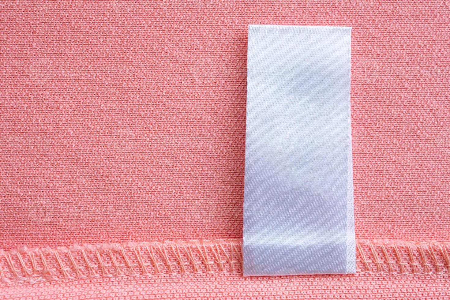 Blank white laundry care clothes label on pink fabric texture background photo