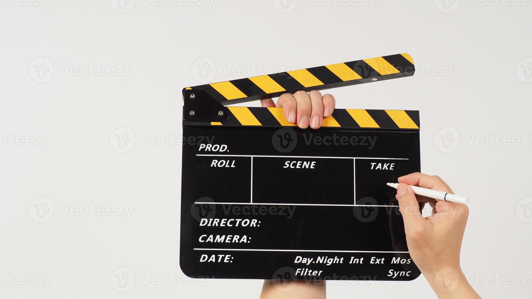 The hand is holding a yellow and black clapper board and marker Pen on black background. photo