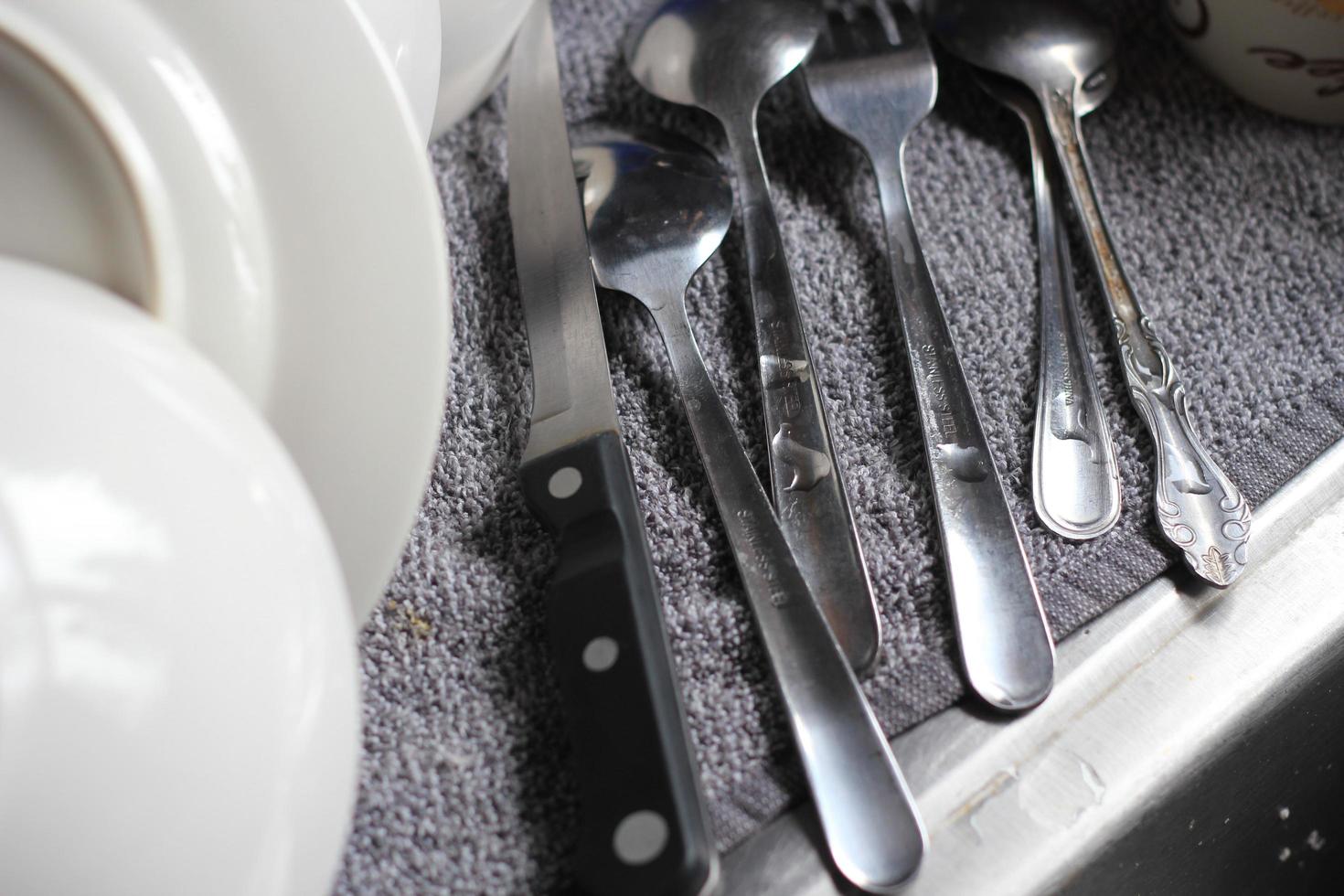 Spoons, fixings, knives and dishes are placed around the sink after washing. photo