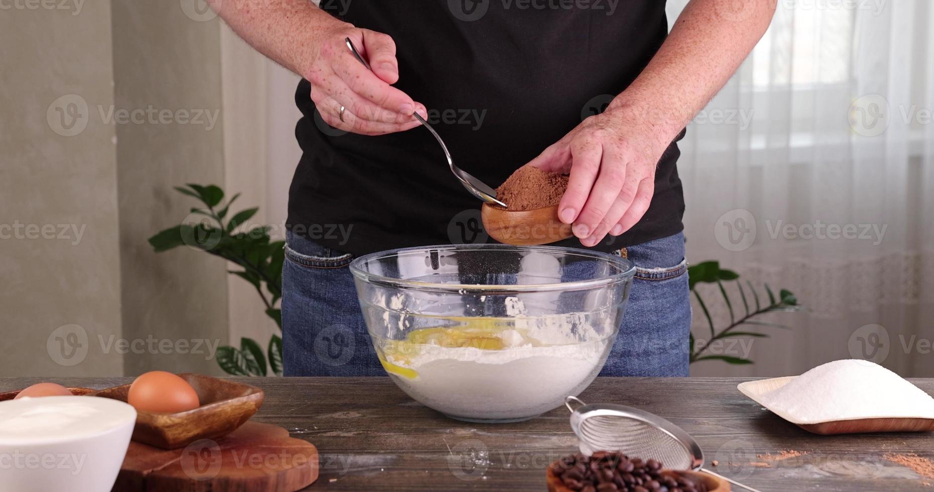 A man pours cocoa in a bowl of flour with sugar while cooking a cake photo