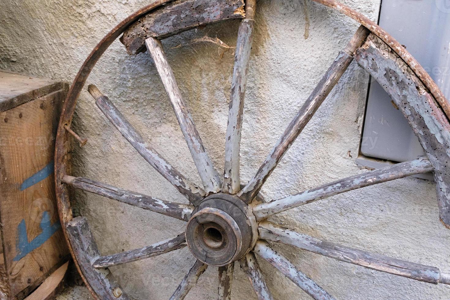 Old wagon wheel in a barn, a wooden carriage wheel against the wall, west handmade old wheel from the cart, a rustic and rural background, simple retro and vintage machine wheels. photo