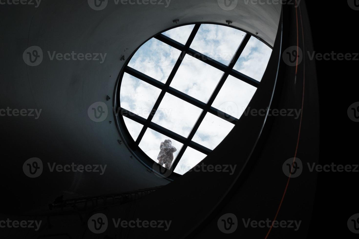 Window in the dark, round glass window in the corridor, floor in the tunnel, metro interior architecture, man standing on the circle glass ceiling against blue sky and white clouds, transparent dome. photo