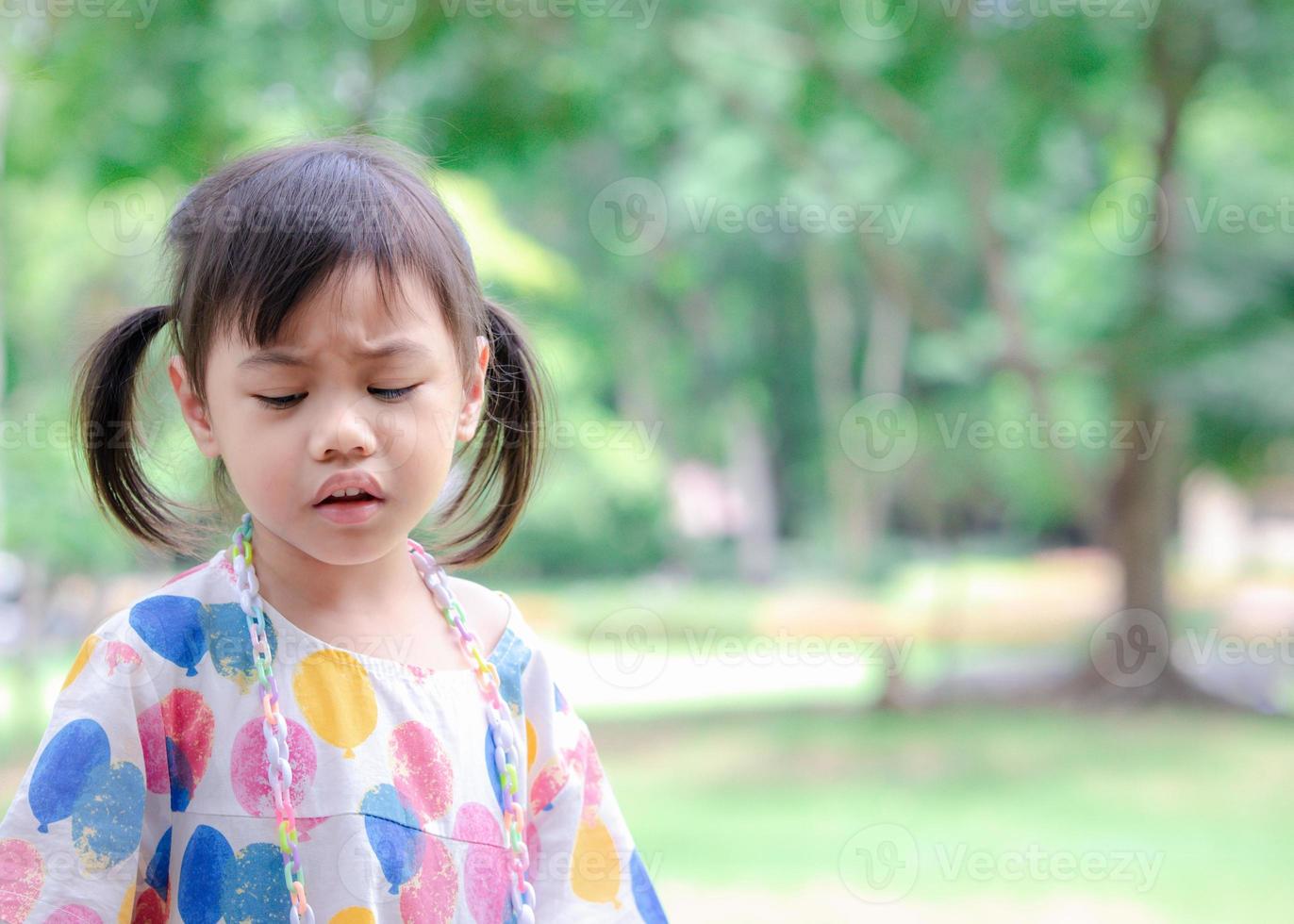 tiro en la cabeza de una linda niña asiática triste de 4 años, un niño pequeño con un adorable pelo de coletas haciendo cara frustrada, mirando hacia abajo con el fondo del espacio de copia. foto