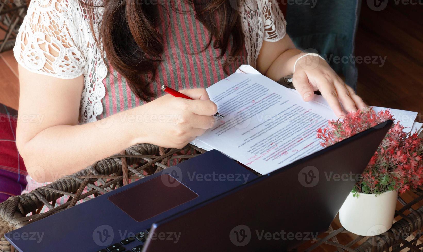 hand holding red pen over blurred paperwork photo