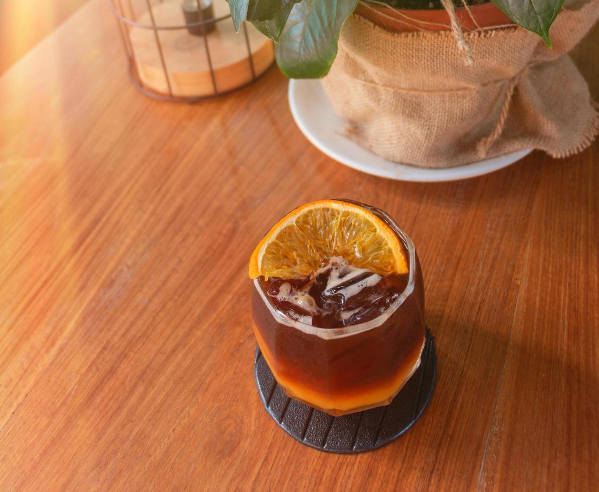 glass of cold black orange coffee on wooden table in cafe photo