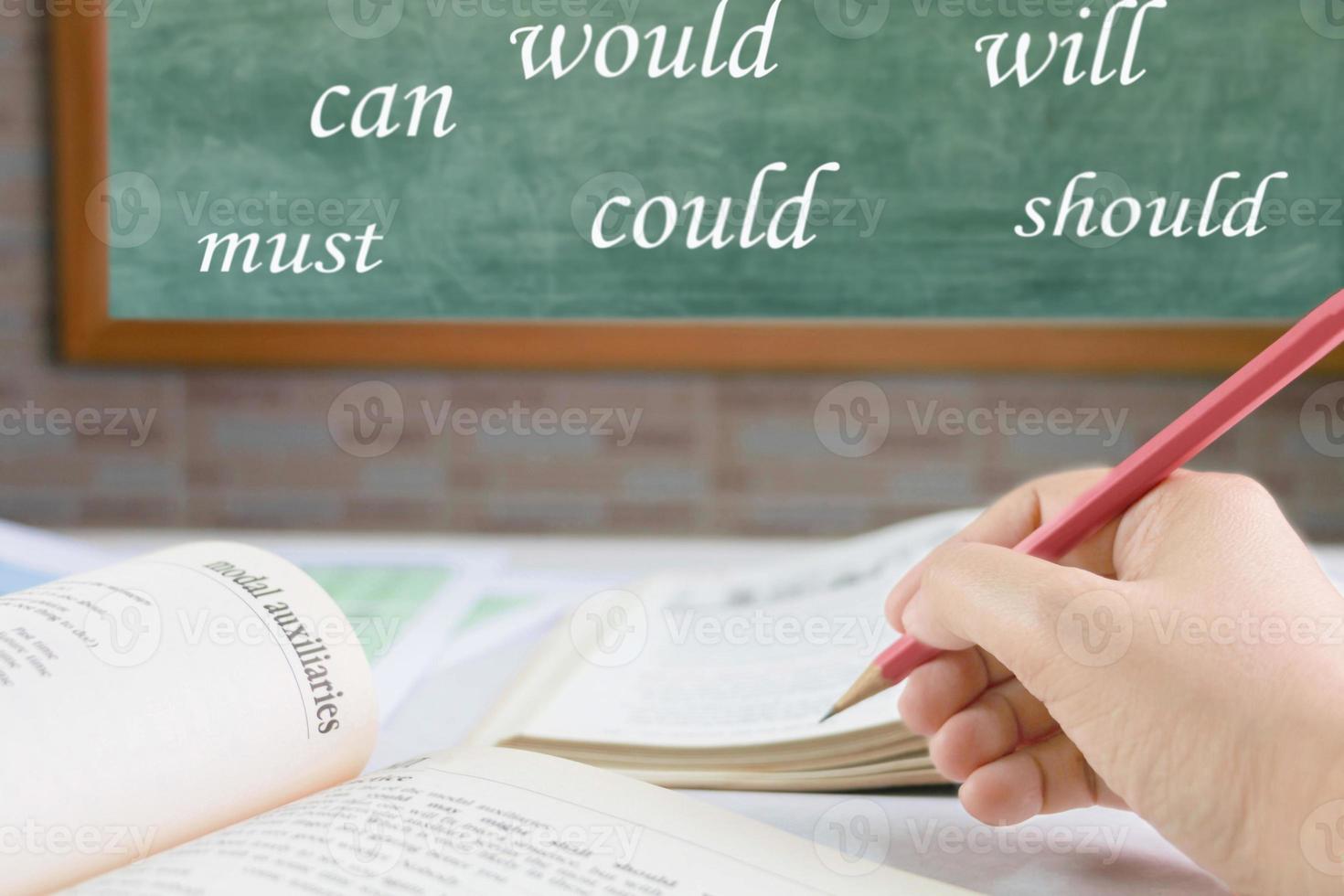 hand holding pencil over blurred textbook on table photo