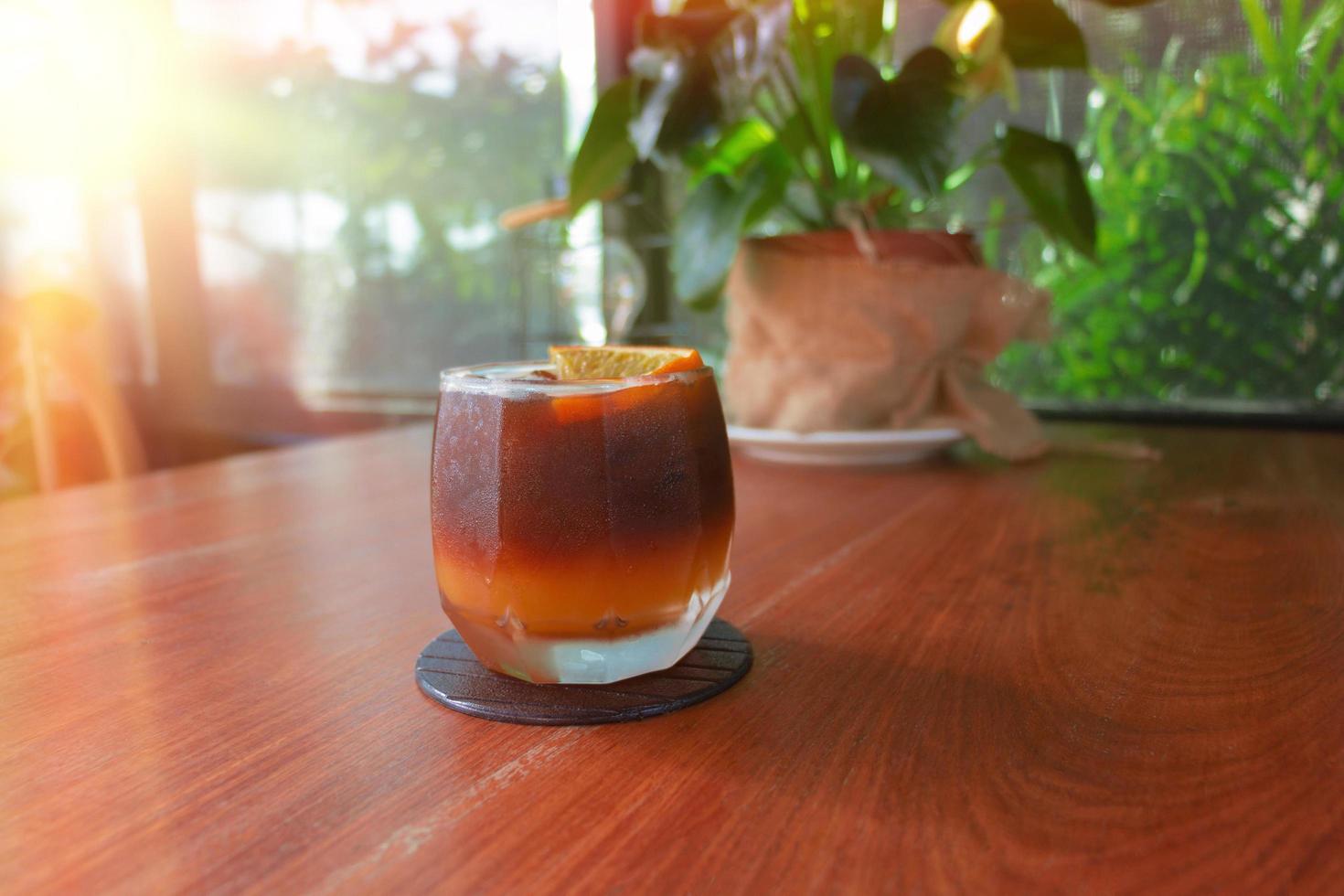 glass of cold black orange coffee on wooden table in cafe photo