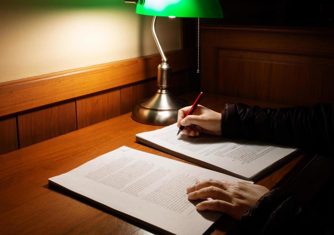 hand holding red pen over blurred proofreading paper on wooden table photo