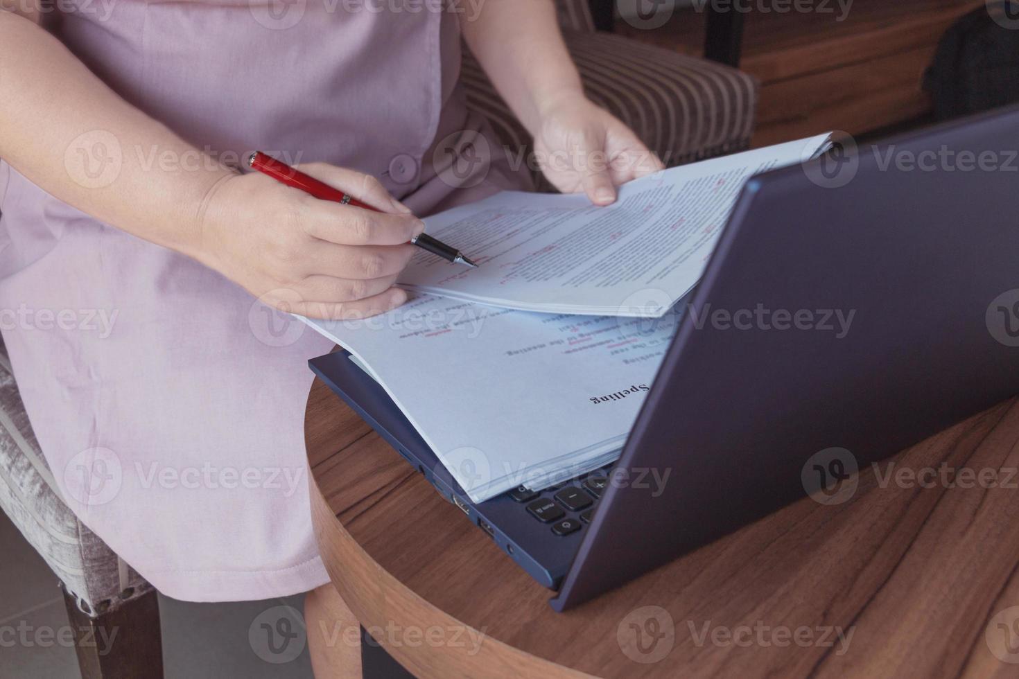 mano de mujer sosteniendo un bolígrafo rojo revisando la ortografía del ensayo foto