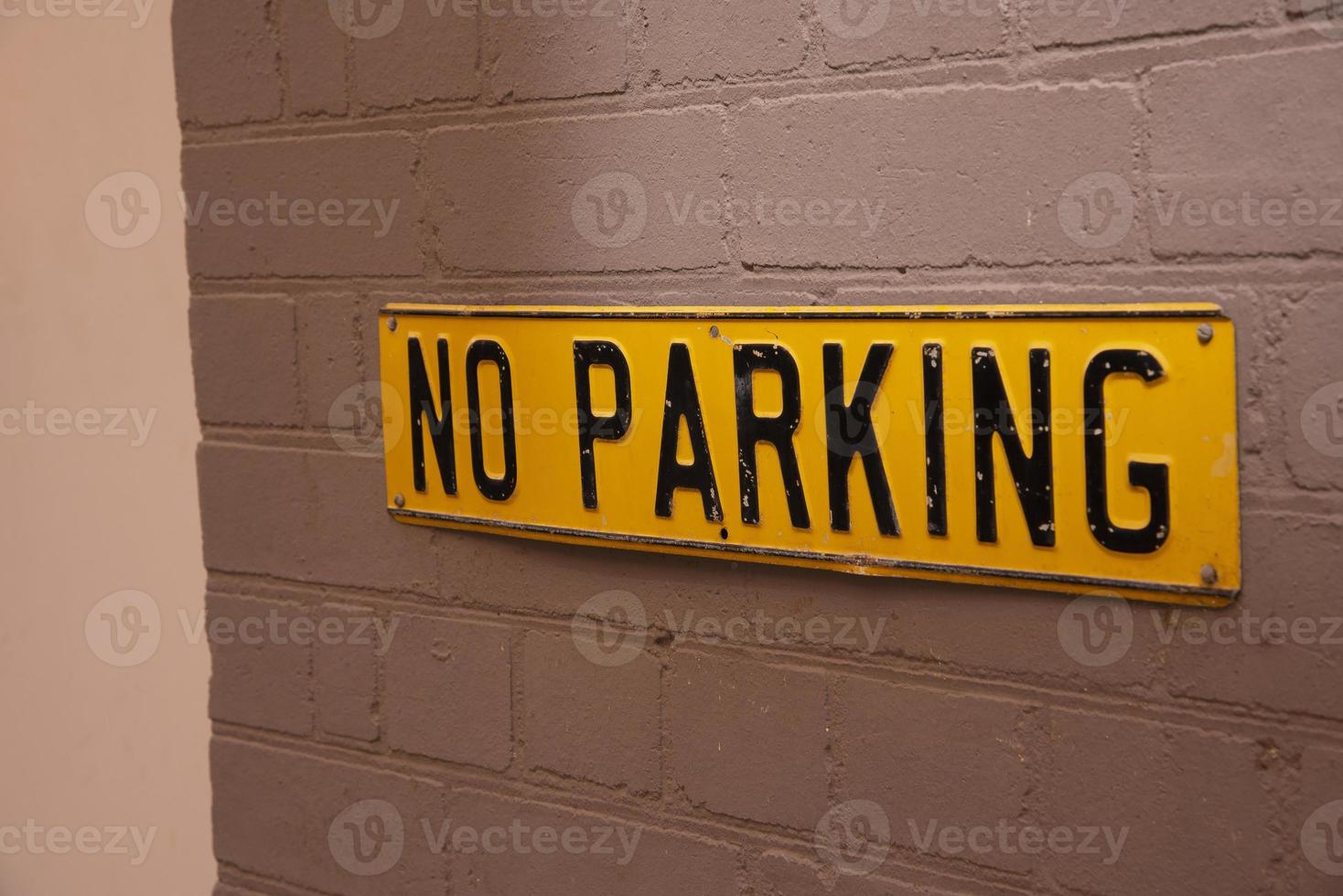 A Square Yellow vintage no parking sign on grey brick wall. photo