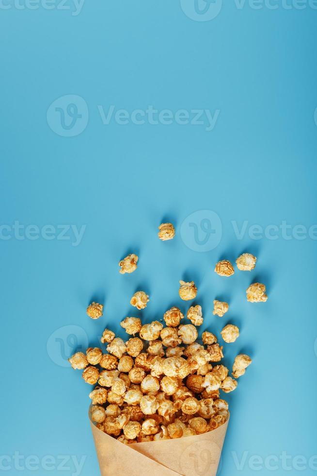 palomitas de maíz en glaseado de caramelo en un sobre de papel sobre un fondo azul. foto