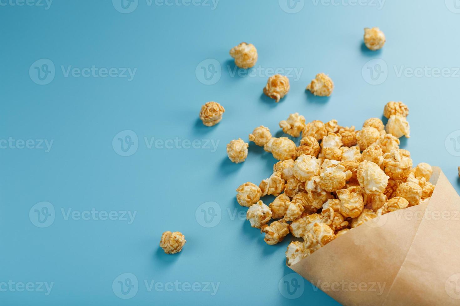 palomitas de maíz en glaseado de caramelo en un sobre de papel sobre un fondo azul. foto