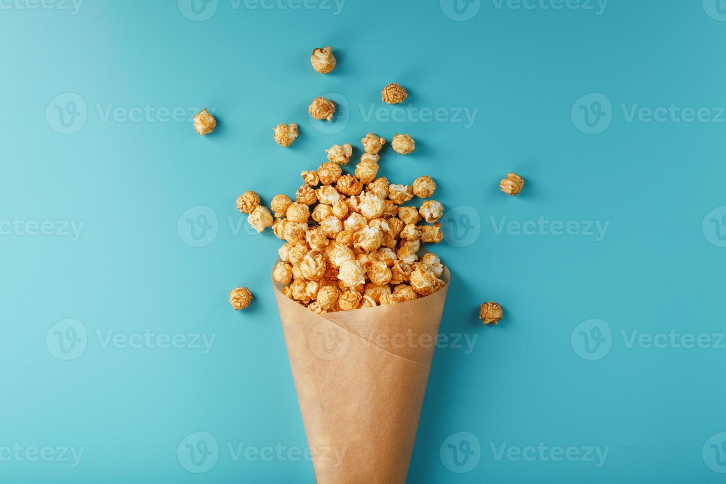 palomitas de maíz en glaseado de caramelo en un sobre de papel sobre un fondo azul. foto