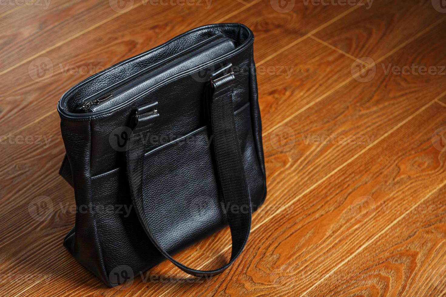 Handmade black leather bag on a wooden background, made of natural material. photo