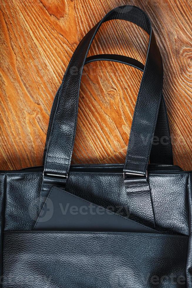 Black notebook peeking out of the pocket of a black leather bag close-up, macro Handmade, natural materials. photo