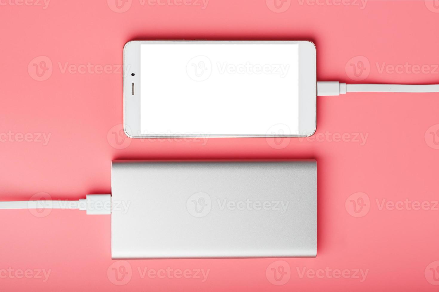 Power Bank charges your smartphone on a pink background. Universal external battery for gadgets free space and minimalistic composition. photo