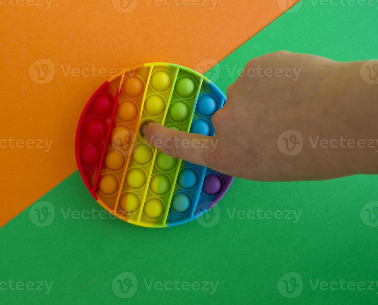 Pop it toy on a green and orange background, a person's hand photo