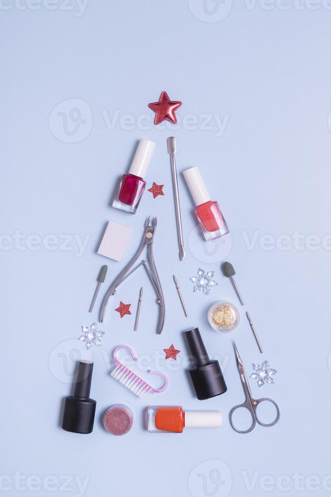 Manicure tools and nail polishes are laid out in the shape of a Christmas tree with copy space on blue background photo