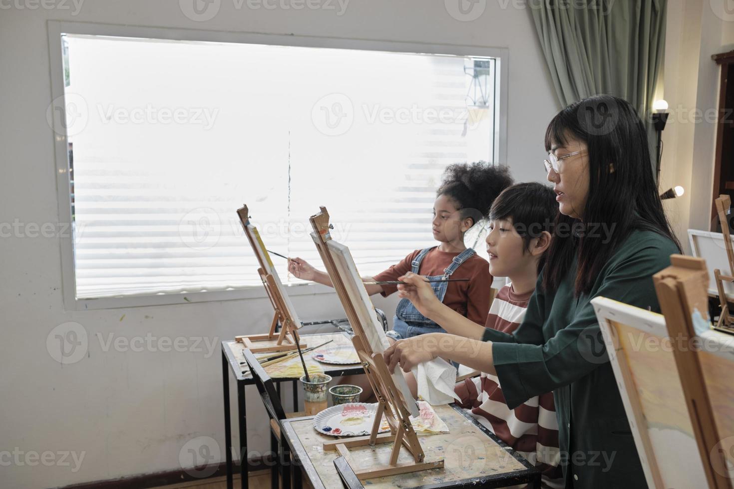 una maestra asiática enseña y demuestra a los niños sobre pintura acrílica en color sobre lienzo en el aula de arte, aprendiendo creativamente con habilidad en la educación de estudio de la escuela primaria. foto