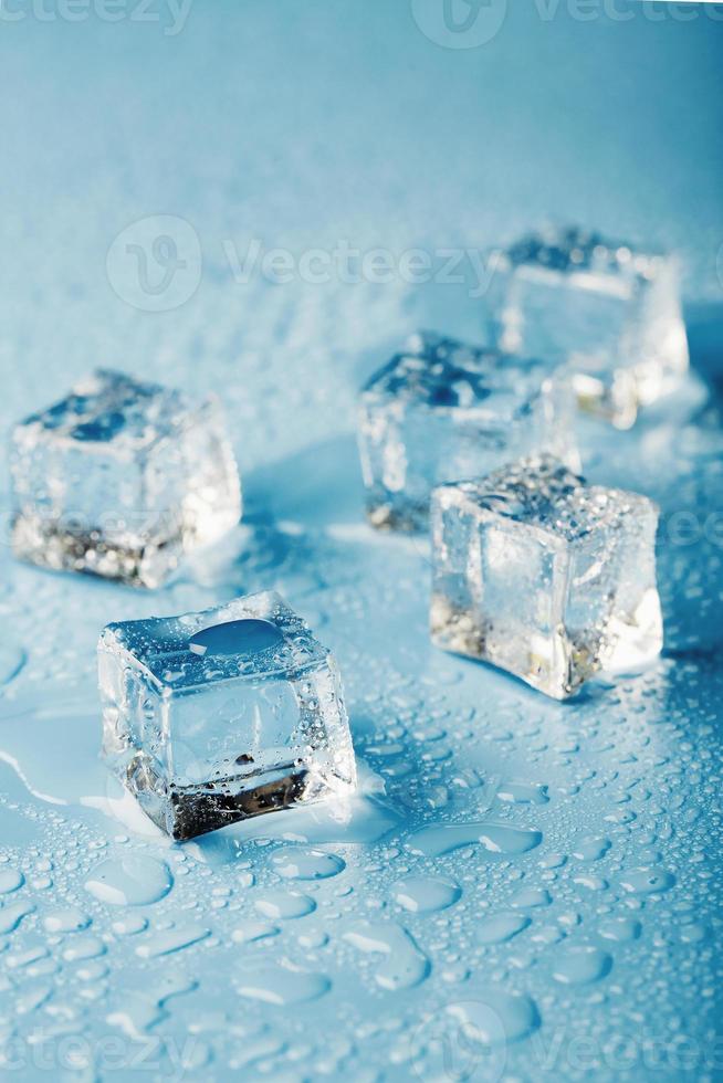 cubos de hielo de primer plano con gotas de agua derretida esparcidas sobre un fondo azul. foto