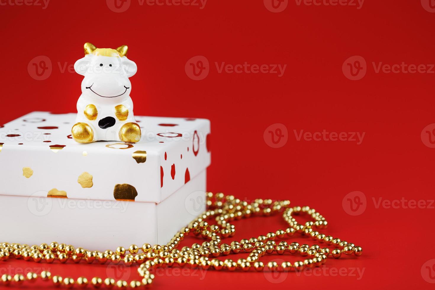 New year's 2021 toy bull with a gift on a red background. Gift box and gold beads. photo