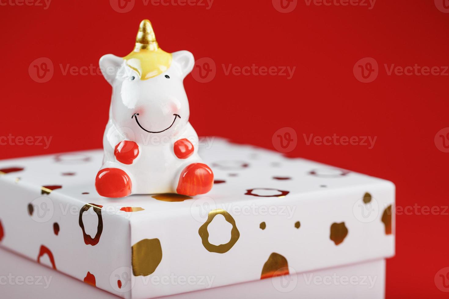 una pequeña figura de un unicornio en la caja con un regalo sobre un fondo rojo. foto