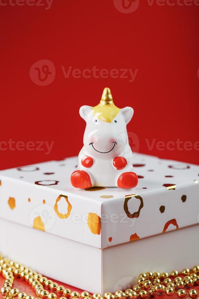 Unicorn figurine on a gift box with gold beads on a red background with free space. photo