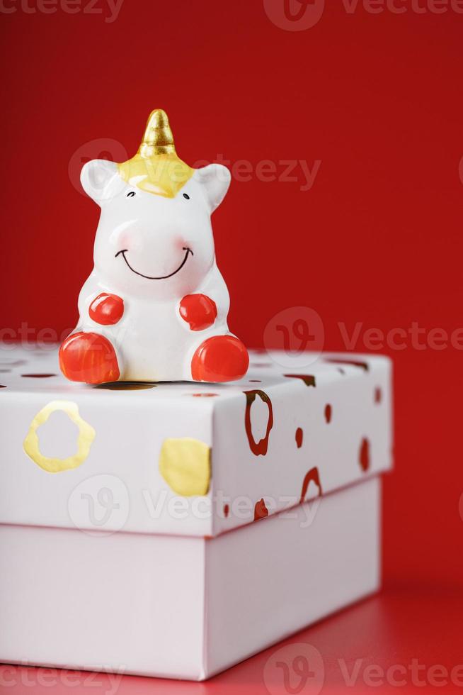 A little figure of a unicorn on the box with a gift on a red background. photo