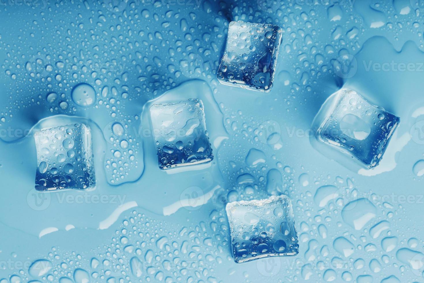 cubos de hielo con gotas de agua derretida sobre un fondo azul, vista superior. foto