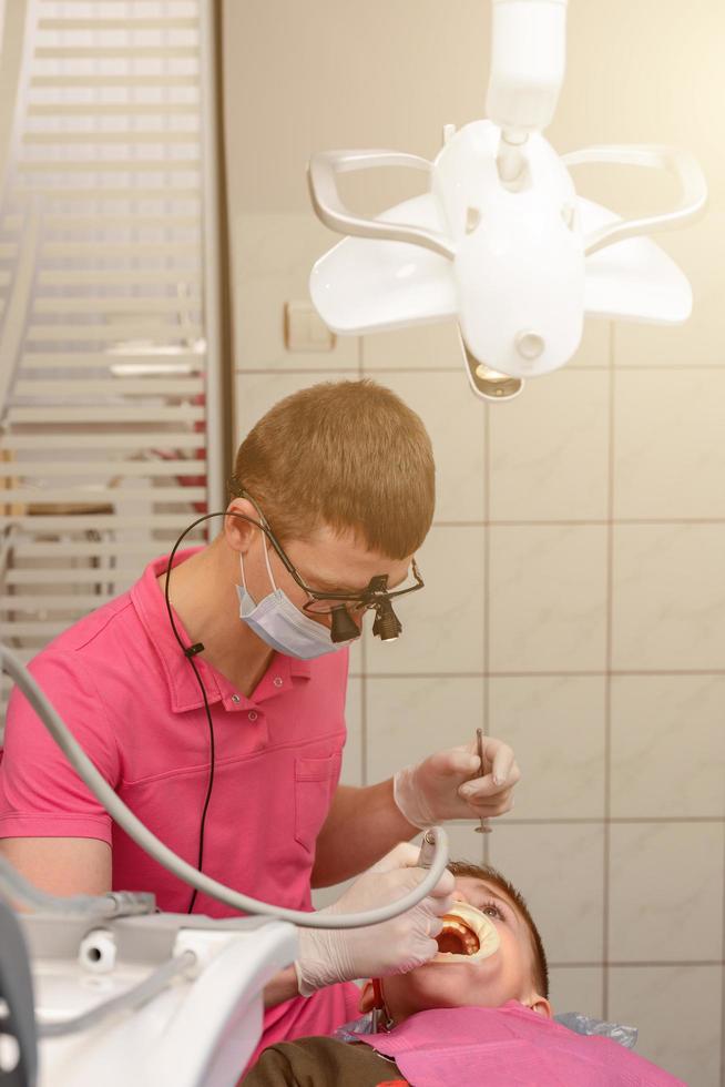 tratamiento dental de un niño, eliminación de caries con un taladro, boca abierta y eyector de saliva. foto